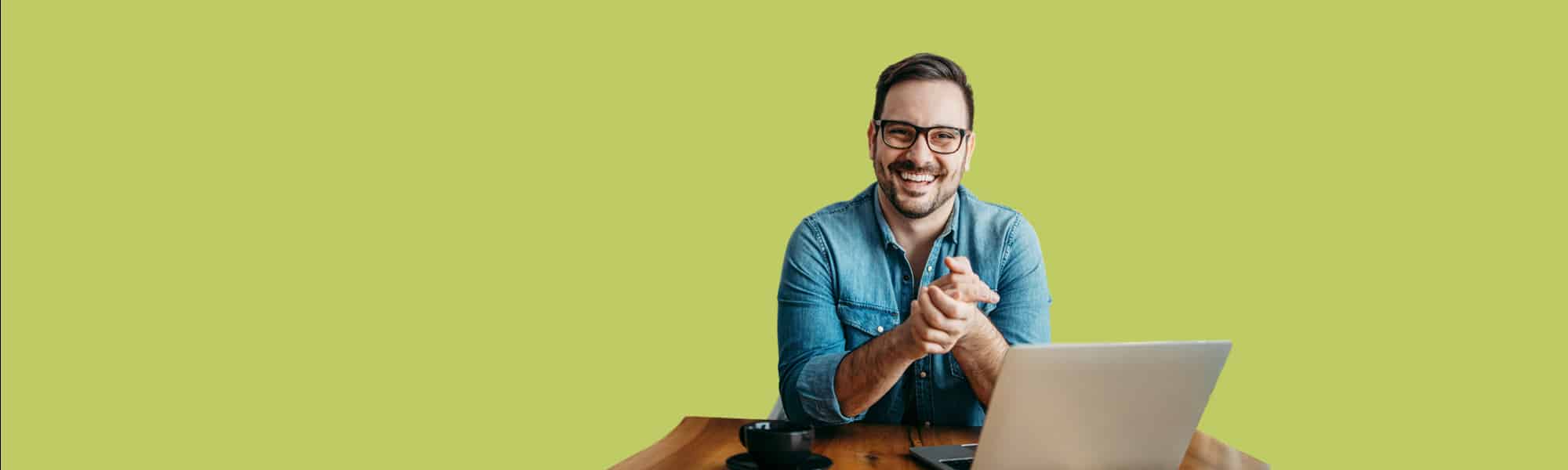 Featured image for blog titled "deciding on the right EDI services". Cut out photo of man smiling with hands together at his home-office desk with laptop open and cup of coffee, bright green backdrop colour to represent Transalis eDI Instant product colour.
