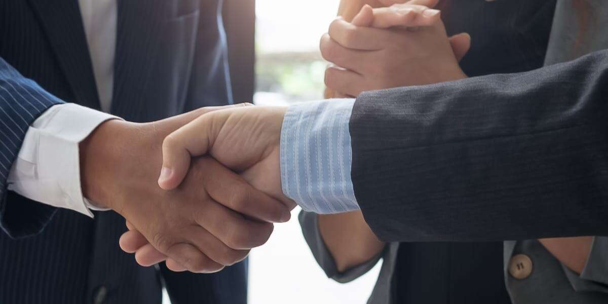 Close-up photo to two corporate businessmen wearing smart suits shaking hands after agreeing a deal. Used to represent blog about strategies for B2B suppliers to secure more market visibility and new customers