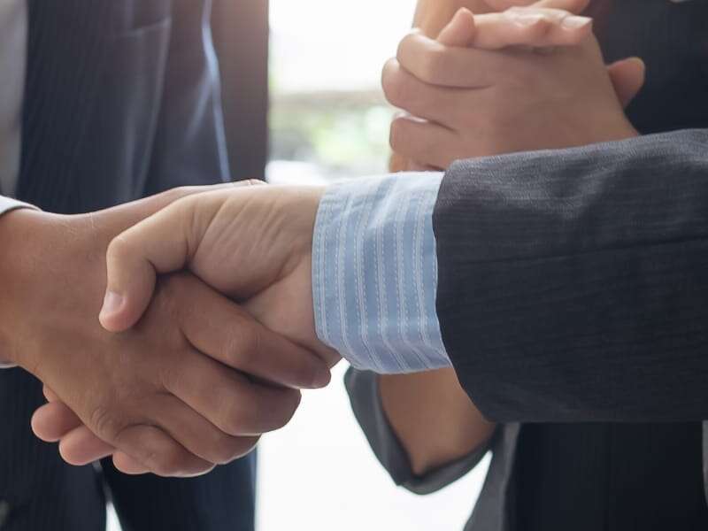 Close-up photo to two corporate businessmen wearing smart suits shaking hands after agreeing a deal. Used to represent blog about strategies for B2B suppliers to secure more market visibility and new customers