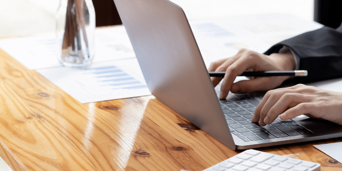 A blog feature image of a male accountant in his office, manually entering data into his laptop, with scattered papers on his desk. This image illustrates the necessity of a Paperless Accounts Payable process