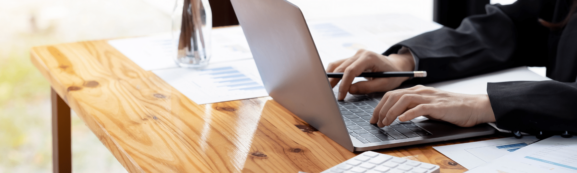 A blog feature image of a male accountant in his office, manually entering data into his laptop, with scattered papers on his desk. This image illustrates the necessity of a Paperless Accounts Payable process