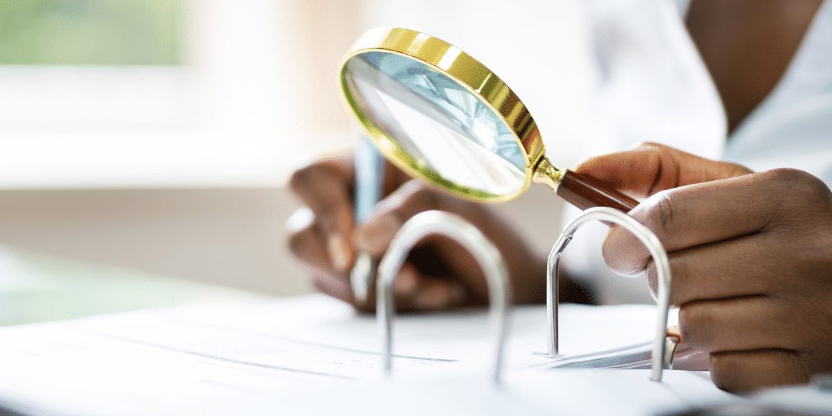 A female accountant is sat by her work desk, looking over a ring binder filled with paper invoices with a magnifying glass. She is trying to manually detect specific information, in particular errors, due to their business' inefficient OCR technology. With IDP technology, Transalis is able to automatically alert and detect errors via the manual exceptions tool