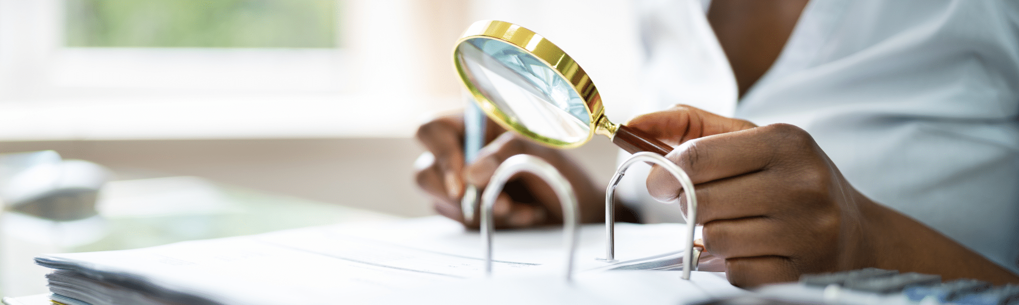 A female accountant is sat by her work desk, looking over a ring binder filled with paper invoices with a magnifying glass. She is trying to manually detect specific information, in particular errors, due to their business' inefficient OCR technology. With IDP technology, Transalis is able to automatically alert and detect errors via the manual exceptions tool