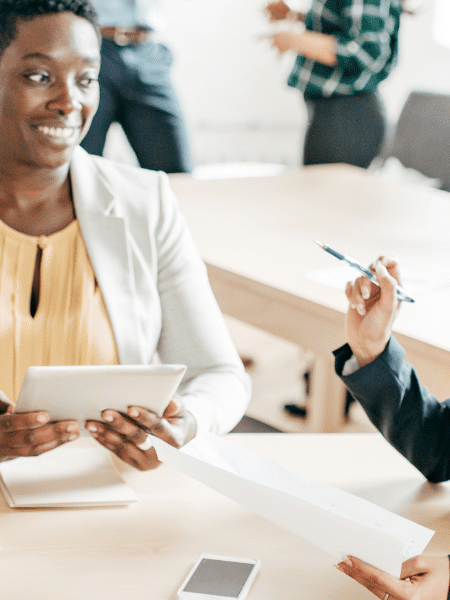A blog feature image shows three female accountants in an office, discussing work whilst holding electronic gadgets. They sit around a desk filled with invoices, symbolising the shift from paper invoices to electronic invoicing software in the AP and AR team.