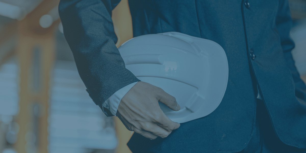 Close up image of a professional holding a hard hat in a warehouse, with a blue tint. Representing the blog titled Cutting costs for a lean supply chain