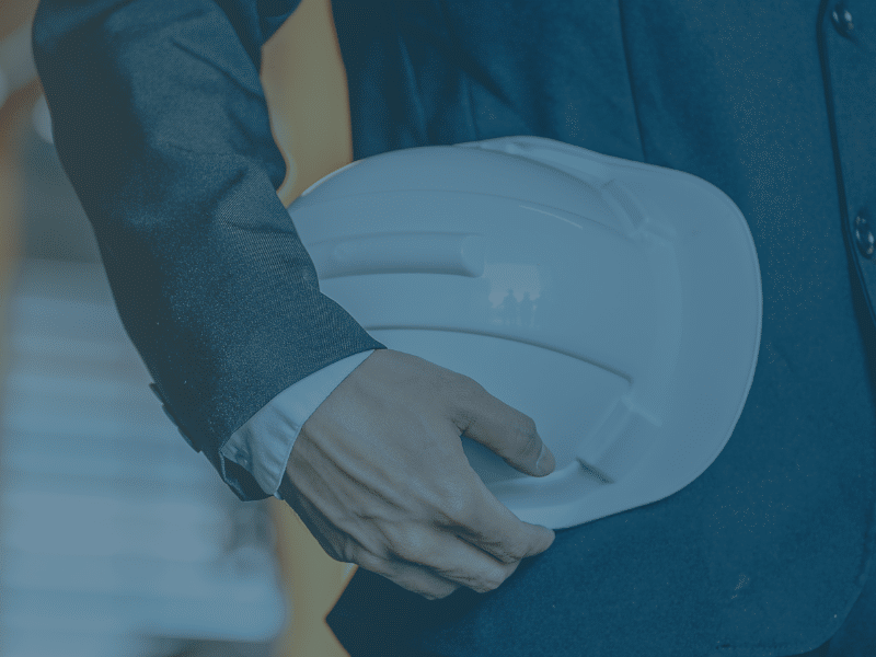 Close up image of a professional holding a hard hat in a warehouse, with a blue tint. Representing the blog titled Cutting costs for a lean supply chain