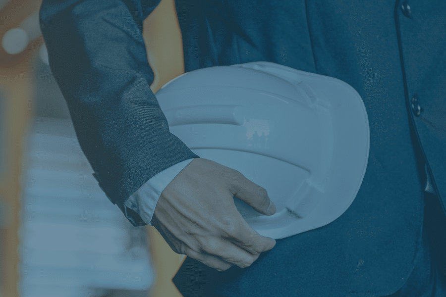 Close up image of a professional holding a hard hat in a warehouse, with a blue tint. Representing the blog titled Cutting costs for a lean supply chain