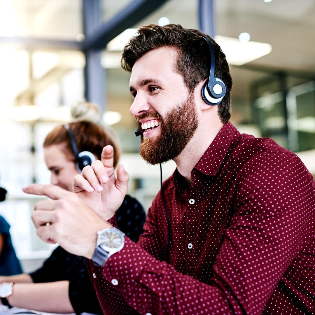 Corporate employee smiling, sitting at his desk and wearing a headset