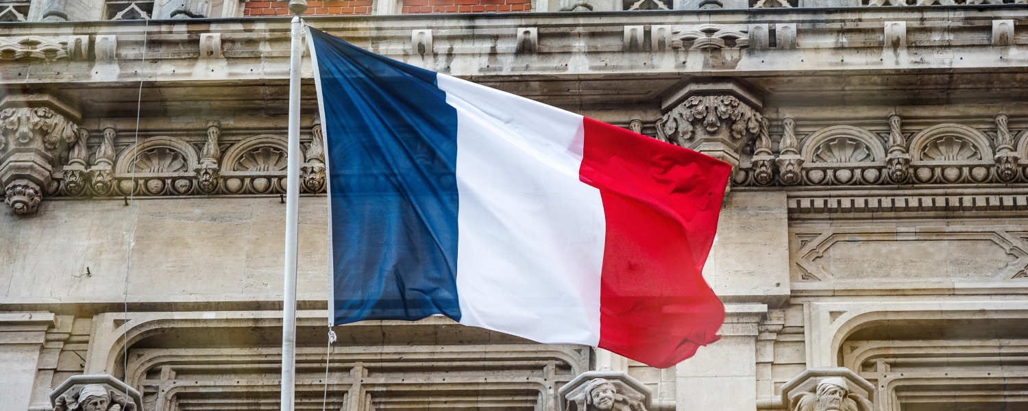 French flag flying full mast in front of an ornate romantic architecture building. Header image for blog titled "France Peppol: reconfirmation eInvoicing deadline."