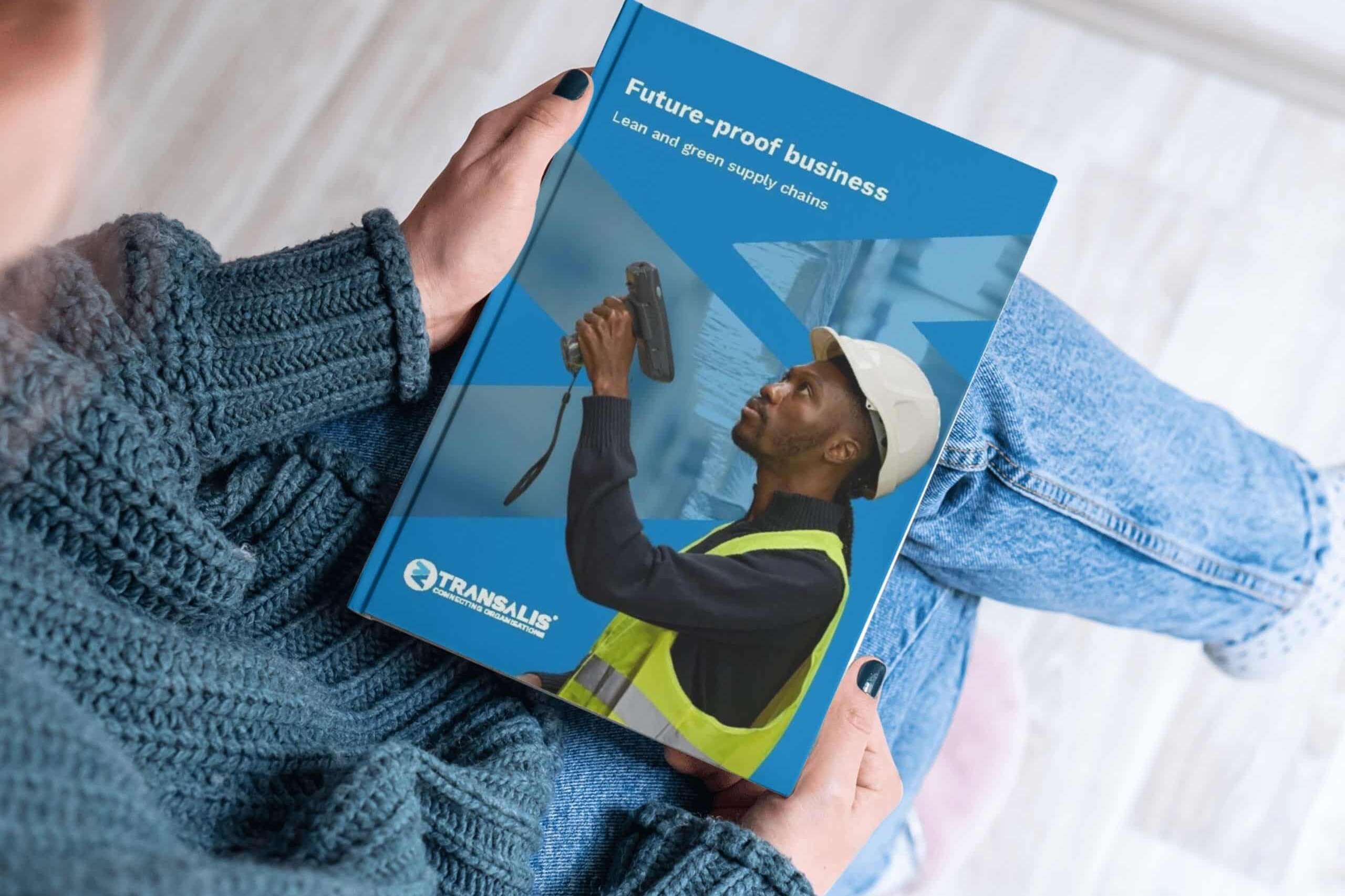 Mockup image of Transalis whitepaper report titled 'Free Report: Build a future-proof business with lean, green supply chain strategies'. Closeup image looking over a woman's shoulder to see her holding the report, looking at the front cover with image of a male warehouse stock manager with a barcode scanner and overlay of Transalis icon logo in blue.