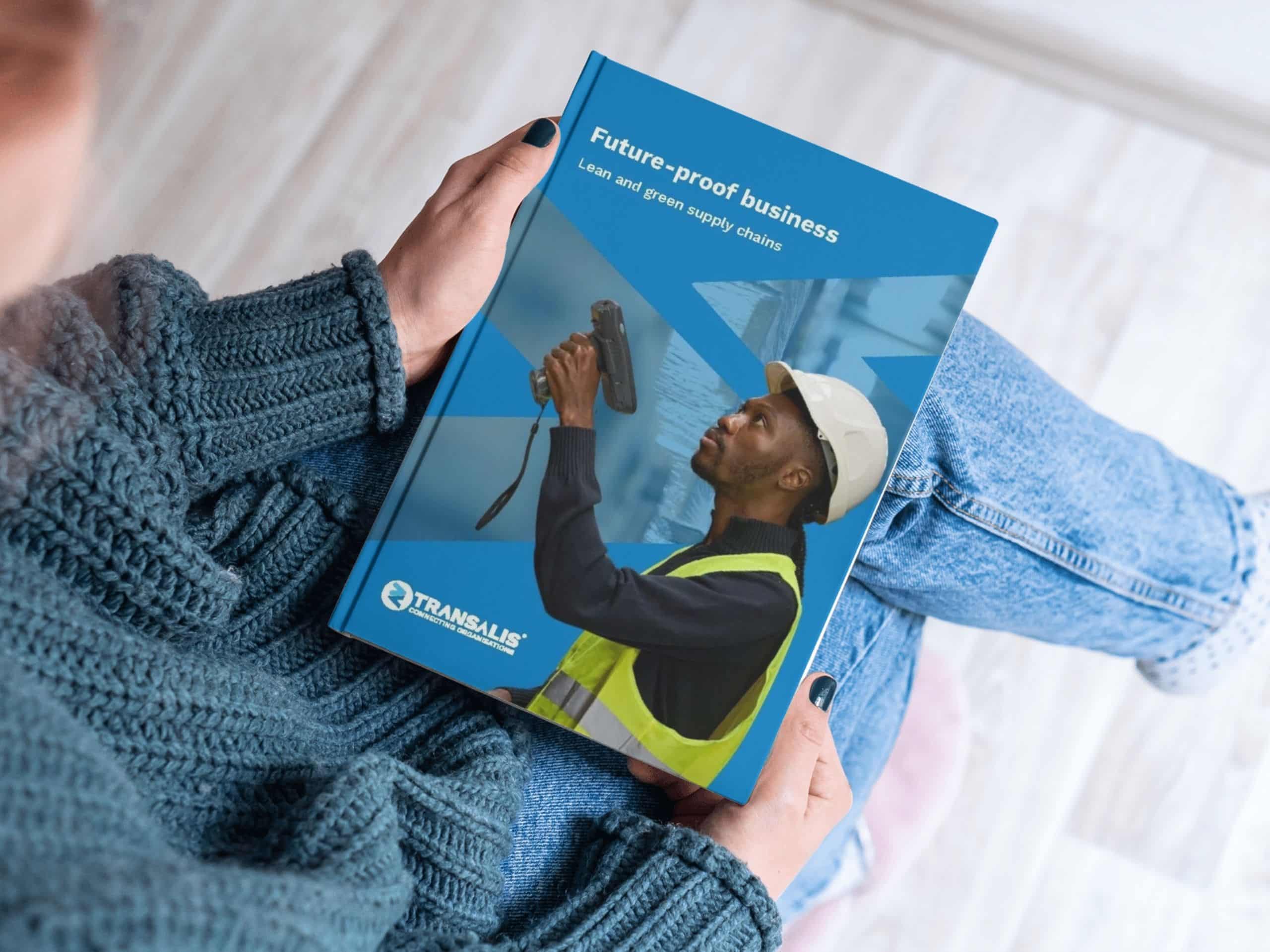 Mockup image of Transalis whitepaper report titled 'Free Report: Build a future-proof business with lean, green supply chain strategies'. Closeup image looking over a woman's shoulder to see her holding the report, looking at the front cover with image of a male warehouse stock manager with a barcode scanner and overlay of Transalis icon logo in blue.