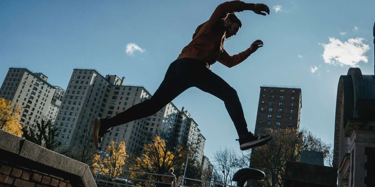 Male parkour runner leaps between buildings in an industrial business complex. Representing a blog post by Transalis, titled: how to achieve business agility