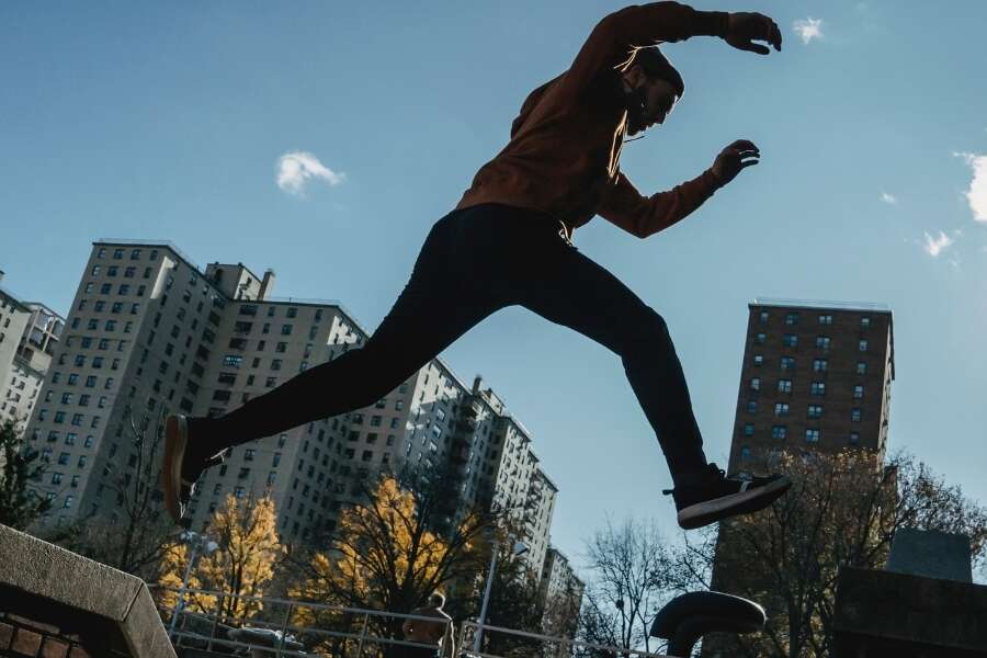 Male parkour runner leaps between buildings in an industrial business complex. Representing a blog post by Transalis, titled: how to achieve business agility