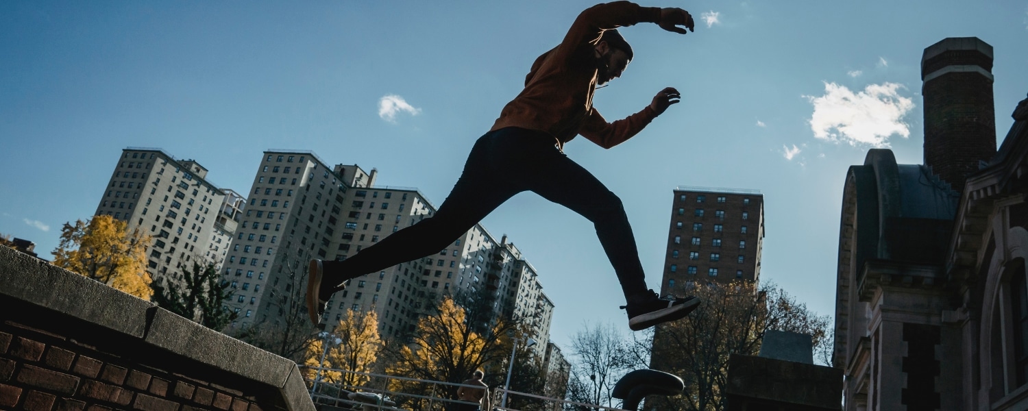 Male parkour runner leaps between buildings in an industrial business complex. Representing a blog post by Transalis, titled: how to achieve business agility
