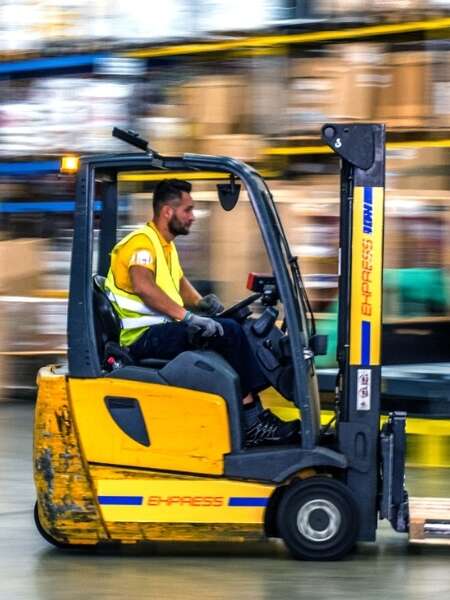 Warehouse worker in high visibility jacket operating a forklift. Surroundings of the warehouse are blurred, implying the forklift is in fast forward-motion. Representing blog titled: The real EDI challenges businesses face with traditional systems