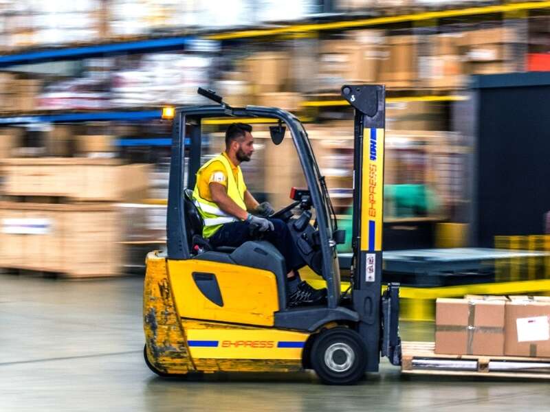Warehouse worker in high visibility jacket operating a forklift. Surroundings of the warehouse are blurred, implying the forklift is in fast forward-motion. Representing blog titled: The real EDI challenges businesses face with traditional systems