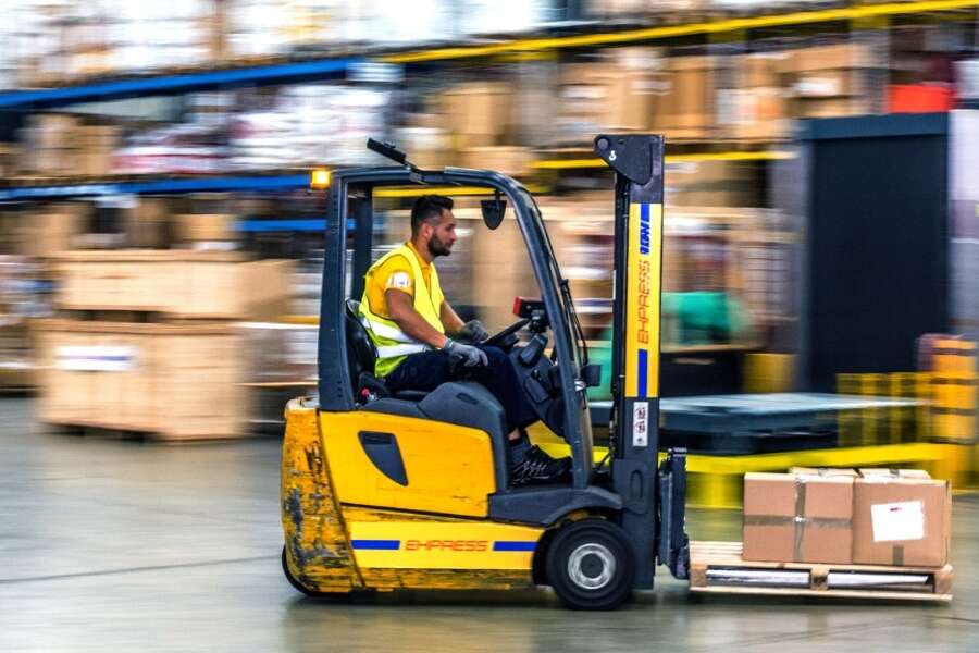 Warehouse worker in high visibility jacket operating a forklift. Surroundings of the warehouse are blurred, implying the forklift is in fast forward-motion. Representing blog titled: The real EDI challenges businesses face with traditional systems