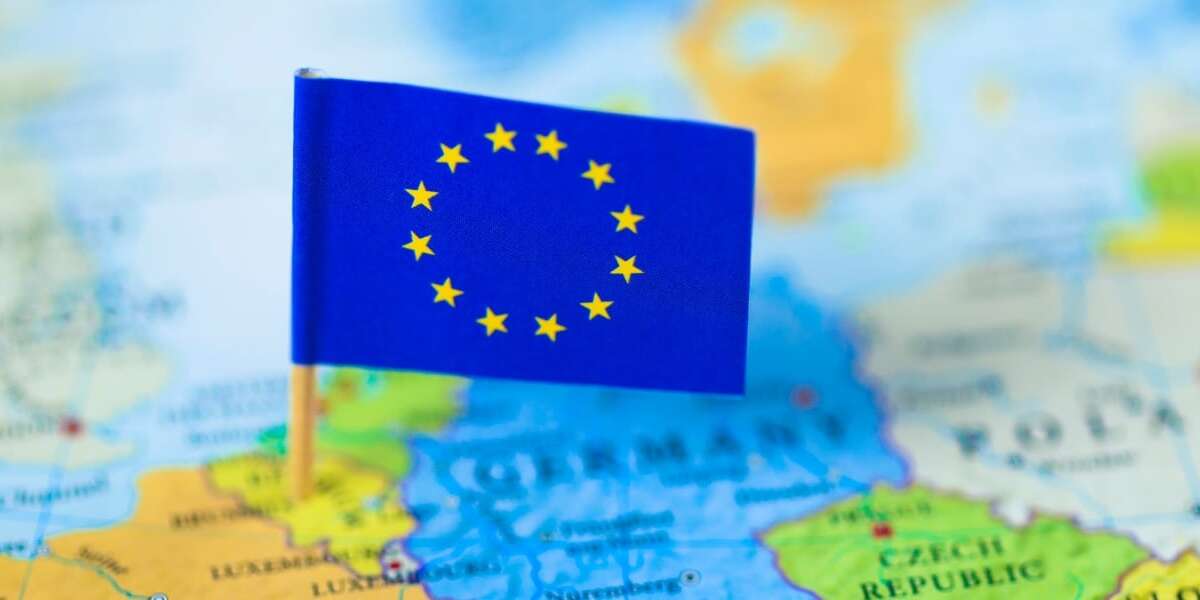 Out of focus map of the continent of Europe in full colour. Mini European flag of stars on cocktail stick in focus and pinned to the location of Brussels in Belgium. Representing the header image of a blog post by Transalis, titled: eInvoicing in Europe: Upcoming deadlines in 2026