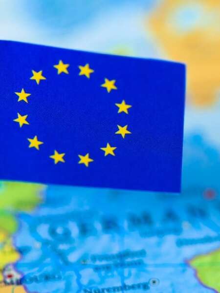 Out of focus map of the continent of Europe in full colour. Mini European flag of stars on cocktail stick in focus and pinned to the location of Brussels in Belgium. Representing the header image of a blog post by Transalis, titled: eInvoicing in Europe: Upcoming deadlines in 2026