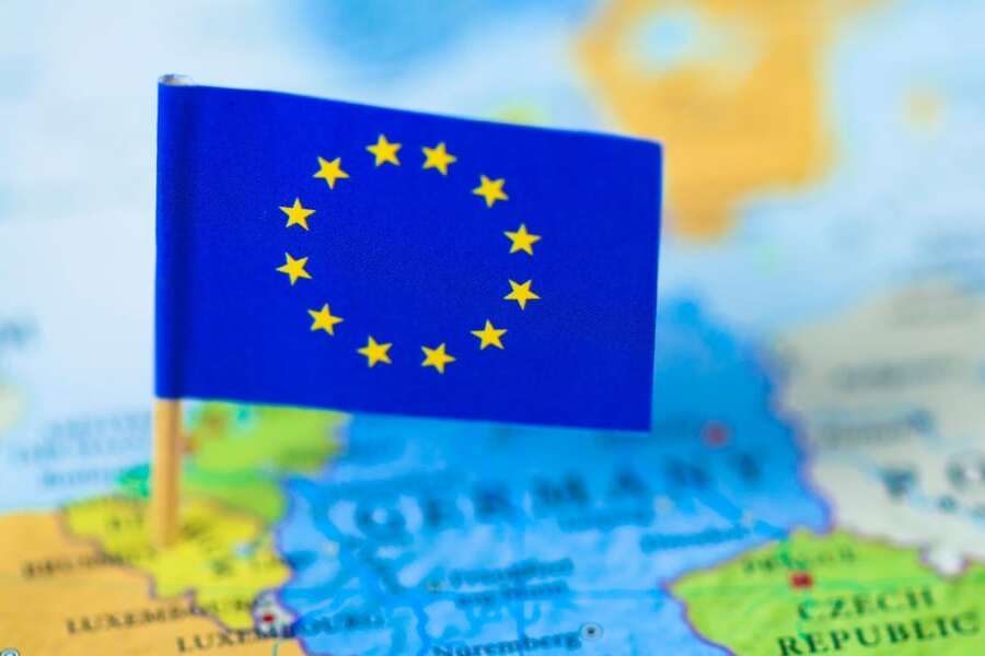 Out of focus map of the continent of Europe in full colour. Mini European flag of stars on cocktail stick in focus and pinned to the location of Brussels in Belgium. Representing the header image of a blog post by Transalis, titled: eInvoicing in Europe: Upcoming deadlines in 2026